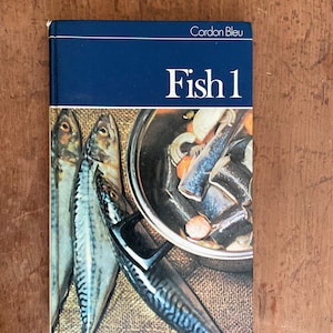 May include: A blue cookbook with the title "Cordon Bleu Fish 1" on the cover. The cover features a photo of a pot of fish and vegetables.