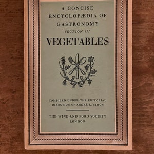 May include: A vintage book cover with a light pink background and a black border. The title is "A Concise Encyclopedia of Gastronomy, Section III: Vegetables". The cover features a black and white illustration of a fork, knife, and spoon crossed over each other with a wheat stalk, grapes, and a flower.