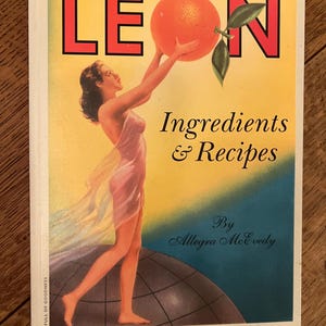 May include: A vintage cookbook cover with a woman holding a large orange. The cover is yellow with the word "LEON" in red letters. The text "Ingredients & Recipes" is in black letters and the author's name "Allegra McEvedy" is in black cursive writing.
