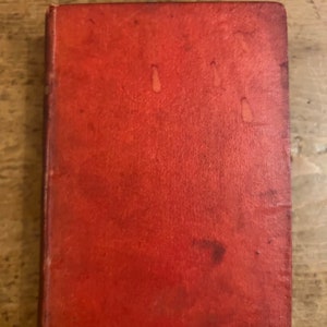 Könnte beinhalten: Ein rot gebundenes Buch mit einem abgenutzten und verblassten Einband.