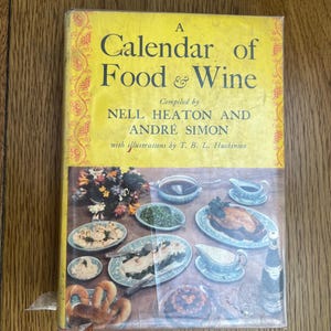 May include: A yellow book titled "A Calendar of Food & Wine" compiled by Nell Heaton and Andre Simon with illustrations by T. B. L. Huskinson. The cover features a vintage illustration of a table setting with food and wine.