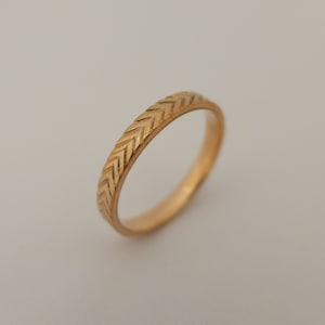 May include: A gold band ring with a chevron pattern.