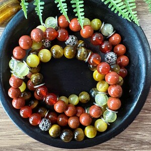 May include: A multi-strand bracelet with red, yellow, and brown beads. The bracelet is made of tiger's eye, red jasper, and aventurine stones.