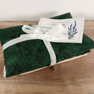 K&ouml;nnte beinhalten: Ein gr&uuml;nes Stoff-W&auml;rmep&auml;ckchen, gebunden mit einem wei&szlig;en Band und einem Etikett mit der Aufschrift "Large Heat & C Made with Flour Rice Wheat" und "Toesera Clean Designs" mit einer Illustration einer Lavendelbl&uuml;te.