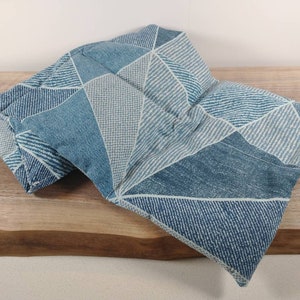 K&ouml;nnte beinhalten: Ein blaues und wei&szlig;es Heizkissen aus Stoff mit geometrischem Muster. Das Kissen ist in der Mitte gefaltet und liegt auf einer Holzoberfl&auml;che.