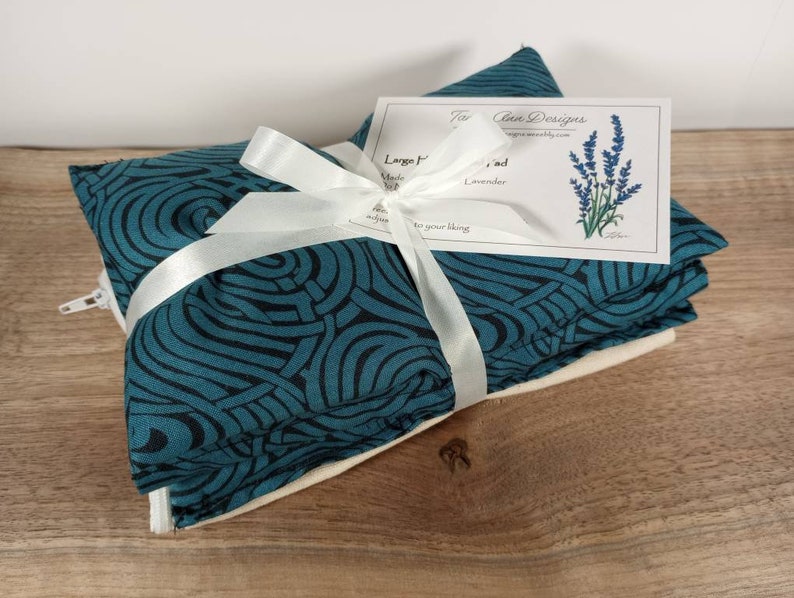 K&ouml;nnte beinhalten: Ein Set aus drei tealblauen und schwarzen W&auml;rmekissen mit Muster, die mit einem wei&szlig;en Band zusammengebunden sind. Die W&auml;rmekissen sind in ein wei&szlig;es Tuch gewickelt und haben einen Rei&szlig;verschluss. Eine kleine Karte mit dem Text "The Clean Designs" ist am Band befestigt.