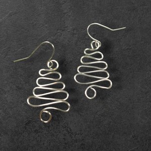May include: A pair of silver wire earrings shaped like Christmas trees. The earrings are simple and elegant, and would make a great gift for any occasion.