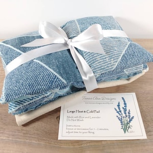 K&ouml;nnte beinhalten: Ein blaues und wei&szlig; gemustertes W&auml;rme- und K&auml;lte-Kissen mit einem wei&szlig;en Band darum gebunden. Das Kissen ist mit Reis und Lavendel gef&uuml;llt und mit "Gro&szlig;es W&auml;rme- und K&auml;lte-Kissen" beschriftet.