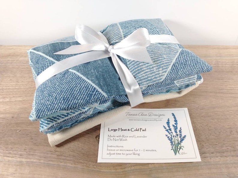 K&ouml;nnte beinhalten: Ein blaues und wei&szlig; gemustertes W&auml;rme- und K&auml;lte-Kissen mit einem wei&szlig;en Band darum gebunden. Das Kissen ist mit Reis und Lavendel gef&uuml;llt und mit "Gro&szlig;es W&auml;rme- und K&auml;lte-Kissen" beschriftet.