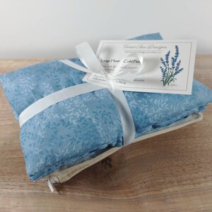 K&ouml;nnte beinhalten: Ein blauer und wei&szlig;er W&auml;rmekissen mit Blumenmuster, das mit einem wei&szlig;en Band umwickelt ist. Das Kissen ist mit "Large Heat Cold Pack Lavender and Rice" beschriftet.