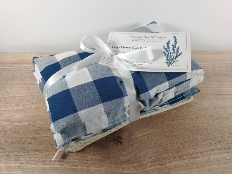 K&ouml;nnte beinhalten: Ein Set aus drei blauen und wei&szlig;en karierten W&auml;rme- und K&auml;ltepacks, die mit einem wei&szlig;en Band zusammengebunden sind. Die Packs sind mit "Large Heat & Cold Pack" beschriftet und zeigen eine Lavendel-Illustration.