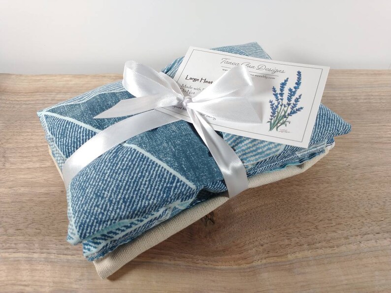 K&ouml;nnte beinhalten: Ein blaues und wei&szlig; gemustertes W&auml;rmekissen, das mit einem wei&szlig;en Band umwickelt und mit einer Schleife gebunden ist. Das W&auml;rmekissen ist mit einer wei&szlig;en Karte verpackt, auf der "Larger Heat Pack" und "Tanessa Rae Designs" steht.