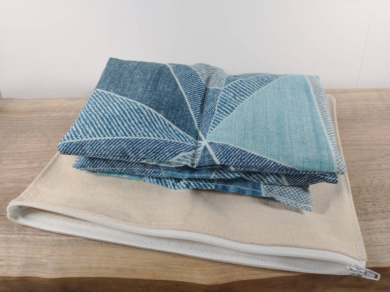 K&ouml;nnte beinhalten: Ein blaues und wei&szlig;es geometrisches Stoff-Augenkissen mit einer Rei&szlig;verschluss-Tasche aus beigefarbener Leinwand.