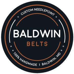 May include: A black and white logo with the text "CUSTOM NEEDLEPOINT" in a circle around the text "BALDWIN BELTS" with the text "100% HANDMADE I BALDWIN. MD" in a circle around the bottom.