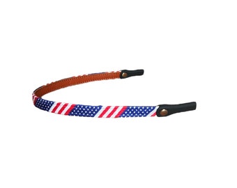 May include: A red, white, and blue patterned glasses strap with brown leather ends and black adjustable buckles.