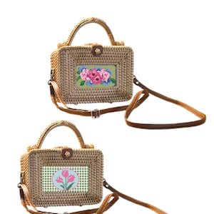 Könnte beinhalten: Zwei rechteckige Handtaschen aus geflochtenem Rattan mit braunen Ledergriffen und verstellbaren Schulterriemen. Die obere Tasche hat einen rechteckigen Aufnäher mit rosa und blauen Blumen. Die untere Tasche zeigt einen runden Aufnäher mit drei rosa Tulpen.