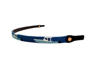 May include: A blue and white patterned strap with a black leather end and a gold button. The strap features a small boat design.