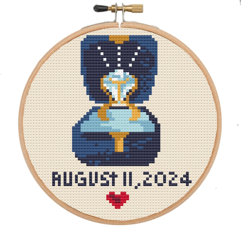 May include: A cross-stitch pattern of a ring in a blue box with a diamond, a heart, and the text "AUGUST 11, 2024".