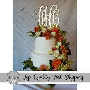 May include: A three-tiered wedding cake decorated with white frosting and fresh flowers. The cake is topped with a gold monogram cake topper.