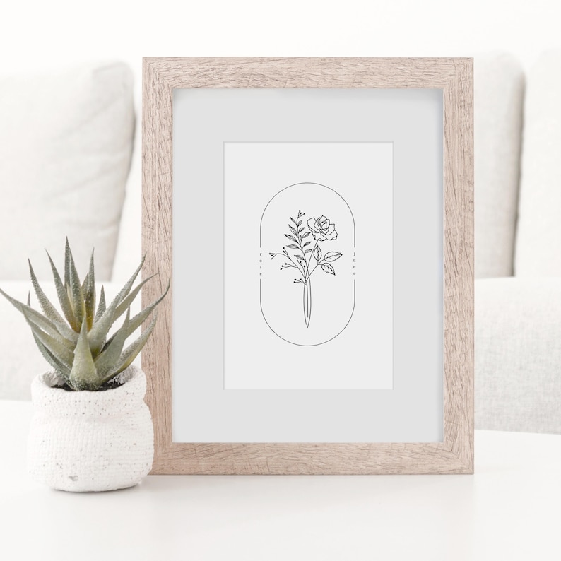 May include: A black and white line drawing of a rose and foliage in an oval frame. The drawing is in a light wood frame.