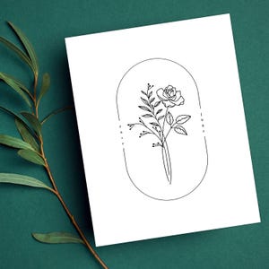 May include: A black and white line drawing of a rose with leaves and buds inside an oval frame. The text "rose" and "june" are written vertically on either side of the frame.