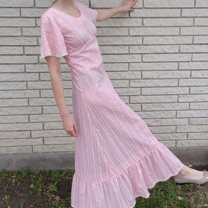 May include: A pink and white striped maxi dress with a ruffled hem and short sleeves. The dress has a white lace trim around the neckline and sleeves.