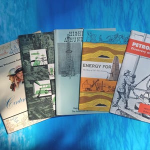 May include: A collection of vintage books on a blue background. The books feature illustrations and text related to the petroleum industry. Titles include "Petroleum Discovery and Production" and "Energy For". The books are from the American Petroleum Institute.