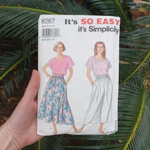 May include: A vintage sewing pattern titled "It's SO EASY it's Simplicity." The pattern features illustrations of two outfits: a pink top with a floral skirt and a striped top with white pants. The pattern number is 8267.