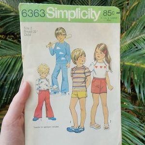 May include: Vintage Simplicity sewing pattern 6363 for children's clothing. The pattern features illustrations of children in various outfits, including pants, shorts, and shirts. The pattern size is 2, with a 21-inch breast measurement. The price is 85 cents.