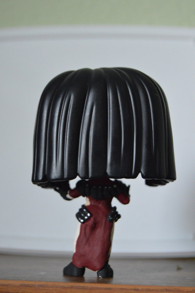 以下が含まれることがあります： 黒と赤のビニール製のフィギュアで、大きな黒い頭と赤と黒の衣装を着ています。フィギュアは木製の表面に立っています。