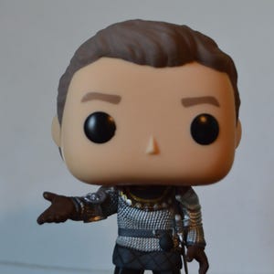 May include: A Funko Pop vinyl figure of a character in silver armour with a brown hairstyle. The figure has a neutral expression and is posed with one arm extended. The figure is a collectible item.