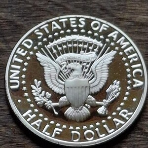 K&ouml;nnte beinhalten: Eine silberne Half-Dollar-M&uuml;nze mit detailliertem Design. Die M&uuml;nze tr&auml;gt die Aufschrift "UNITED STATES OF AMERICA" und "HALF DOLLAR". In der Mitte ist ein Adler mit ausgebreiteten Fl&uuml;geln zu sehen, der Pfeile und einen Olivenzweig h&auml;lt.