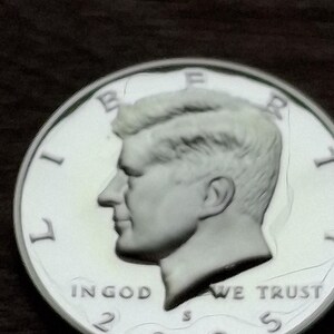 K&ouml;nnte beinhalten: Nahaufnahme einer silbernen Kennedy-Halbdollar-M&uuml;nze von 2005. Die M&uuml;nze zeigt ein Profil von John F. Kennedy und die Worte "IN GOD WE TRUST". Die M&uuml;nze befindet sich auf einem dunklen Hintergrund.