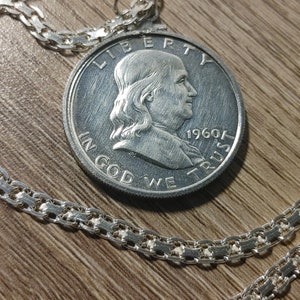 Puede incluir: Un collar de cadena de plata con un colgante de moneda de plata que presenta un perfil de Benjamin Franklin y la inscripción "Liberty, In God We Trust, 1960".