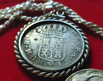 May include: A silver pendant necklace with a silver coin featuring a coat of arms and the text "DUD.M.R. HISPANIA", surrounded by a rope-like border.