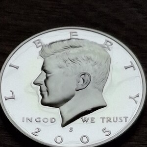 K&ouml;nnte beinhalten: Eine silberne Kennedy-Halbdollar-M&uuml;nze von 2005. Die M&uuml;nze zeigt ein Profil von John F. Kennedy mit den Inschriften "LIBERTY", "IN GOD WE TRUST" und "UNITED STATES OF AMERICA". Die M&uuml;nze ist rund und hat ein detailliertes Design.