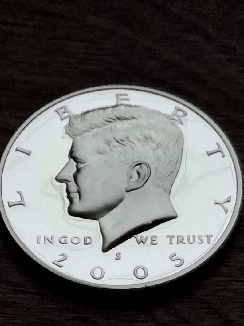 K&ouml;nnte beinhalten: Eine silberne Kennedy-Halbdollar-M&uuml;nze von 2005. Die M&uuml;nze zeigt ein Profil von John F. Kennedy mit den Inschriften "LIBERTY", "IN GOD WE TRUST" und "UNITED STATES OF AMERICA". Die M&uuml;nze ist rund und hat ein detailliertes Design.