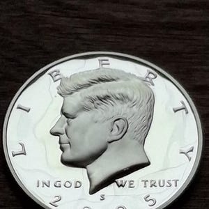 K&ouml;nnte beinhalten: Eine silberne Kennedy-Halbdollar-M&uuml;nze von 2003. Die M&uuml;nze zeigt ein Profil von John F. Kennedy und die Inschriften "LIBERTY", "IN GOD WE TRUST" und "UNITED STATES OF AMERICA". Die M&uuml;nze ist rund und silberfarben.