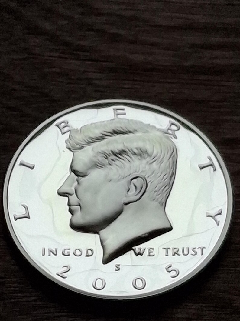 K&ouml;nnte beinhalten: Eine silberne Kennedy-Halbdollar-M&uuml;nze von 2003. Die M&uuml;nze zeigt ein Profil von John F. Kennedy und die Inschriften "LIBERTY", "IN GOD WE TRUST" und "UNITED STATES OF AMERICA". Die M&uuml;nze ist rund und silberfarben.