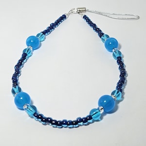 May include: A blue and dark blue beaded phone charm with a silver clasp and four large blue glass beads.