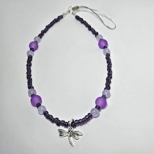 May include: A purple and white beaded phone charm with a silver dragonfly pendant.