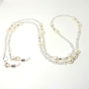 May include: A white beaded eyeglass chain with pearl accents and silver clasps. The chain is double-stranded and has a delicate, elegant look.