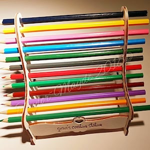 Pode incluir: Porta-lápis de madeira com um recorte em forma de coração e o texto "Grace's Creation Station". O porta-lápis está cheio de lápis de cor em vários tons de azul, verde, amarelo, rosa, vermelho e roxo.