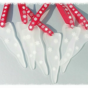 May include: Five white frosted glass icicle ornaments with snowflake designs, each with a red ribbon with white snowflake print.