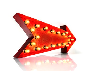 May include: Red arrow sign with light bulbs. The arrow is pointing to the left. The sign is made of metal and has a distressed finish.
