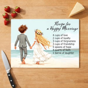 May include: A rectangular cutting board with a beach scene illustration. The image features a couple walking hand-in-hand, with text that reads "Recipe for a Happy Marriage" and a list of ingredients. Strawberries, a knife, and cheese are also present.