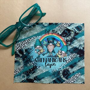 May include: A green microfiber cleaning cloth with a colorful design featuring three cartoon leprechauns holding beer mugs. The text "Let the Shenanigans Begin" is printed on the cloth.