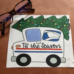 May include: White microfiber cleaning cloth with a colorful illustration of a mail truck carrying a Christmas tree with the text "Tis the Season".