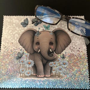 May include: A microfiber cleaning cloth featuring a cartoon elephant with butterflies and flowers. The cloth has a sparkly, glittery background and is paired with a pair of eyeglasses with a tortoiseshell pattern.