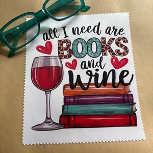 May include: White fabric coaster with a red wine glass, a stack of books, and the text "all I need are BOOKS and wine". The text is in black with red hearts and a leopard print design.